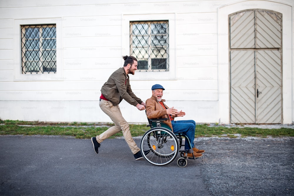 Un jeune homme et son père aîné en fauteuil roulant lors d’une promenade en ville, s’amusant.