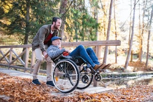 Senior father with wheelchair and his son on walk in nature, having fun.