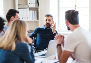 A businessman in wheelchair with colleagues sitting around table, working in a modern office.