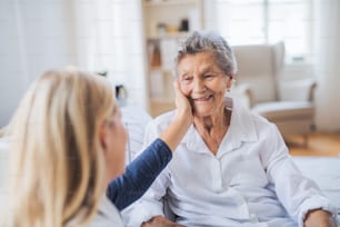 Un giovane visitatore sanitario che parla con una donna anziana malata felice seduta sul letto a casa.