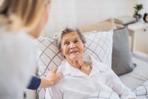 Un joven visitador de salud hablando con una anciana enferma feliz acostada en la cama en casa.