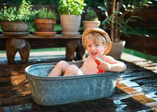 夏に庭の屋外の浴槽に帽子をかぶった幸せな小さな男の子がスイカを食べる。