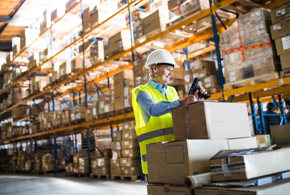 Senior warehouse woman worker or supervisor using a mobile handheld PC with barcode scanner.