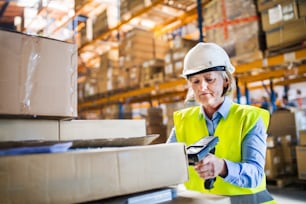 Senior warehouse woman worker or supervisor using a mobile handheld PC with barcode scanner.