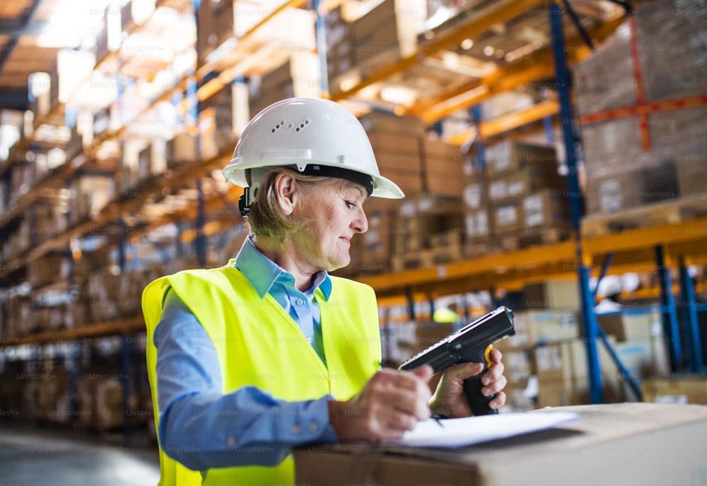 Senior warehouse woman worker or supervisor using a mobile handheld PC with barcode scanner.