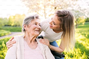 Abuela anciana en silla de ruedas con una nieta adulta afuera en la naturaleza primaveral.