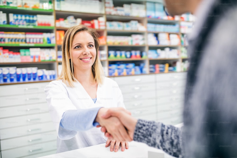 Female friendly pharmacist serving an unrecognizable male customer. A man and woman shaking hands.