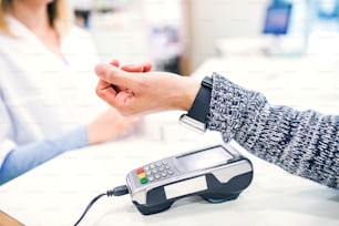 An unrecognizable customer making wireless or contactless payment using smartwatch. Pharmacist accepting payment.