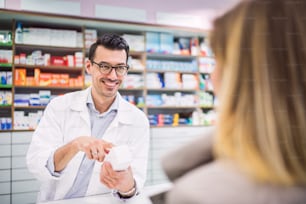 Handsome male friendly pharmacist serving an unrecognizable female customer.