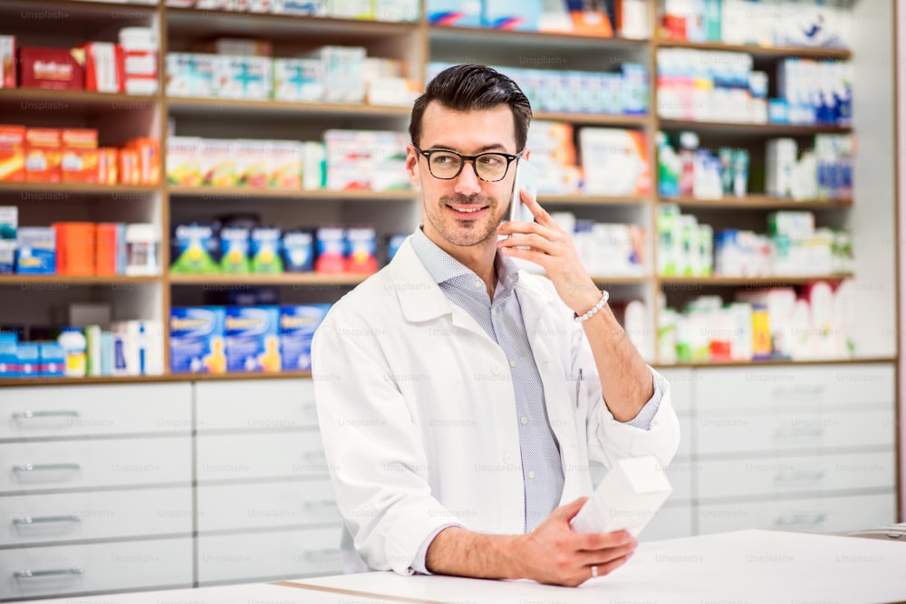 Portrait of a young atrractive friendly male pharmacist with a smartphone. Man making a phone call.
