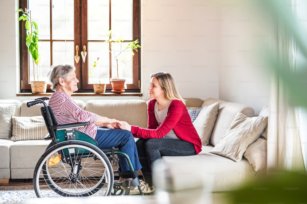 휠체어를 탄 연로한 할머니와 성인 손녀가 집 소파에 앉아 있다.