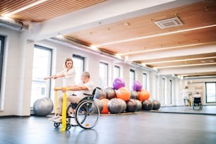 Young attractive woman physiotherapist working with a senior man in wheelchair.