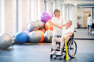 휠체어를 탄 노인과 함께 일하는 젊은 매력적인 여성 물리치료사.