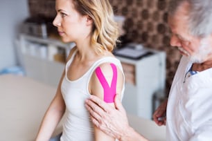 Senior male physiotherapist applying tape on a young female patient.