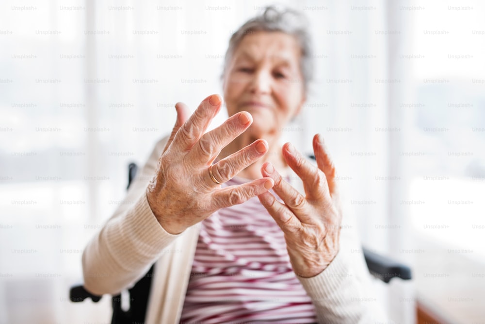 Mujer mayor en silla de ruedas en casa, mirando sus manos.