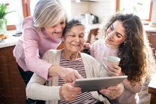 A teenage girl with her mother and grandmother in wheelchair at home, using tablet. Family and generations concept.