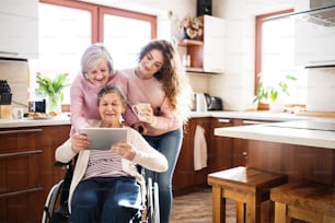 A teenage girl with her mother and grandmother in wheelchair at home, using tablet. Family and generations concept.