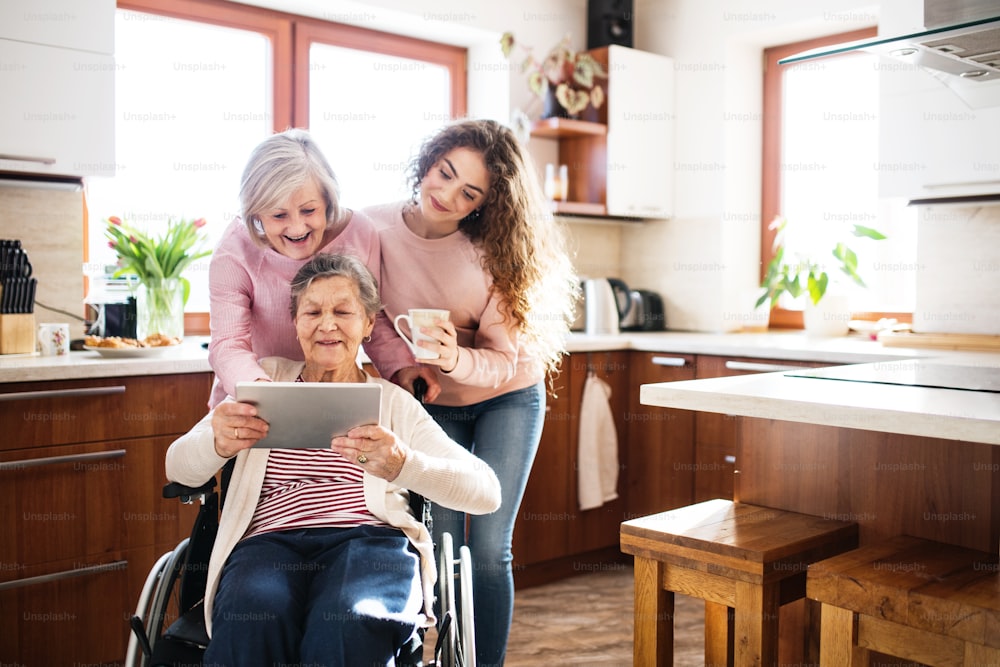 A teenage girl with her mother and grandmother in wheelchair at home, using tablet. Family and generations concept.