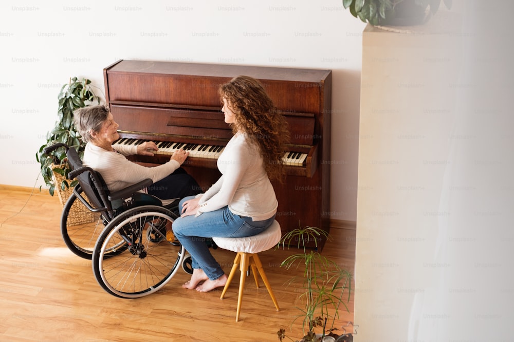 Uma adolescente com avó em cadeira de rodas tocando piano em casa. Conceito de família e gerações. Visão de alto ângulo.