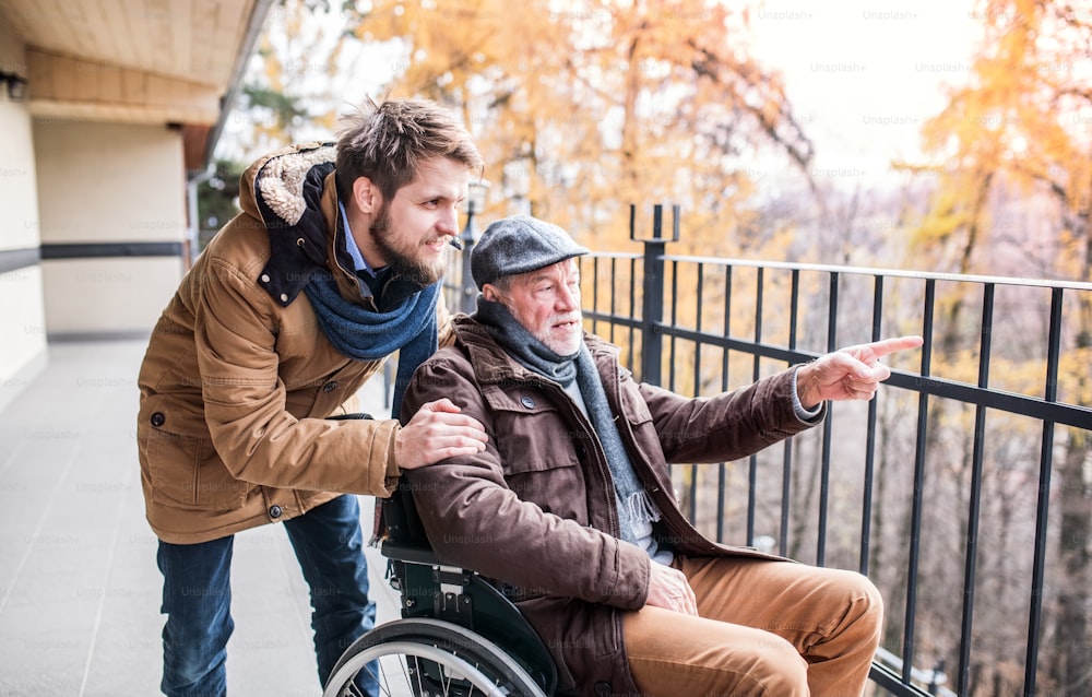 Father in wheelchair and young son on a walk. A carer assisting disabled senior man.