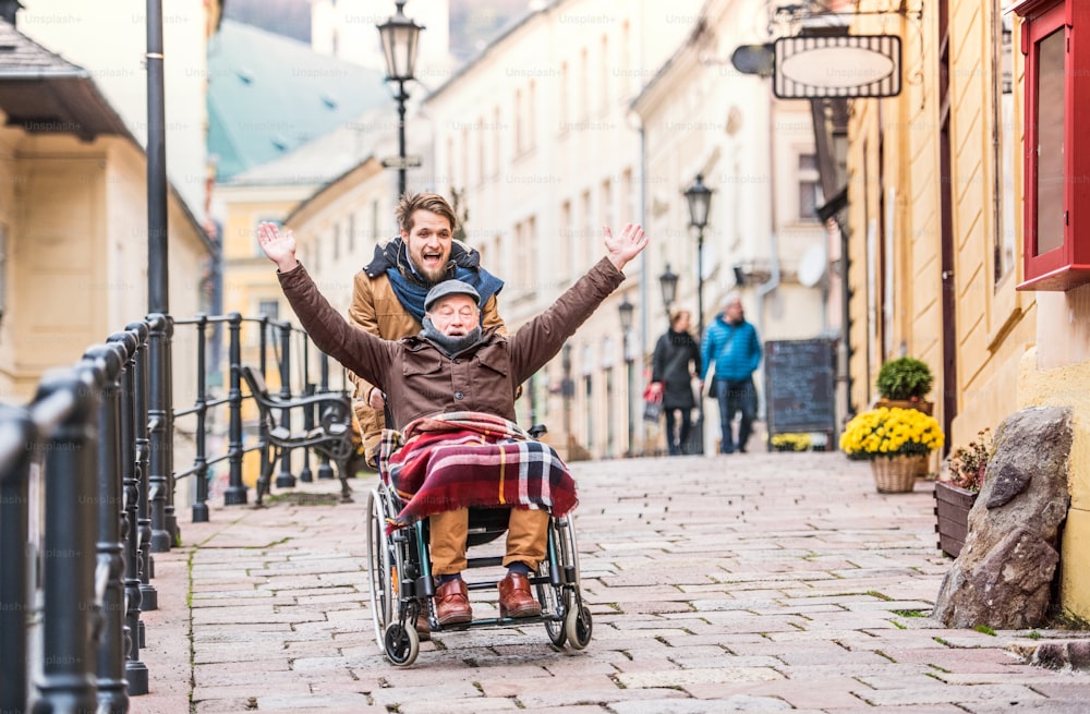 Father in wheelchair and young son on a walk. A carer assisting disabled senior man.