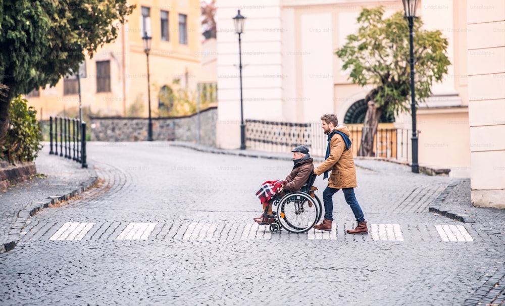 Father in wheelchair and young son on a walk. A carer assisting disabled senior man.