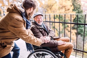 Father in wheelchair and young son on a walk. A carer assisting disabled senior man.