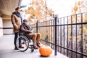 Padre en silla de ruedas e hijo pequeño en un paseo. Un cuidador que asiste a un anciano discapacitado.