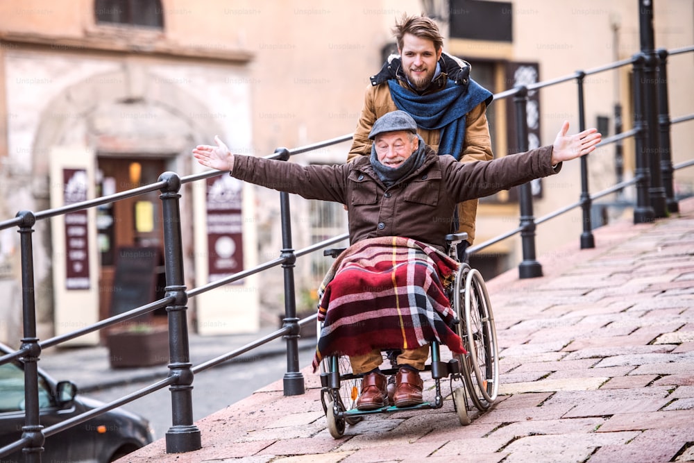 휠체어를 탄 아버지와 어린 아들이 산책을 하며 즐거운 시간을 보내고 있습니다. 장애인 노인을 돕는 간병인.