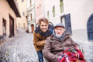 Father in wheelchair and young son on a walk. A carer assisting disabled senior man.