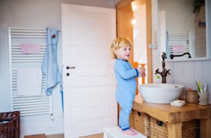 Bambino sveglio in piedi su uno sgabello davanti allo specchio in bagno.