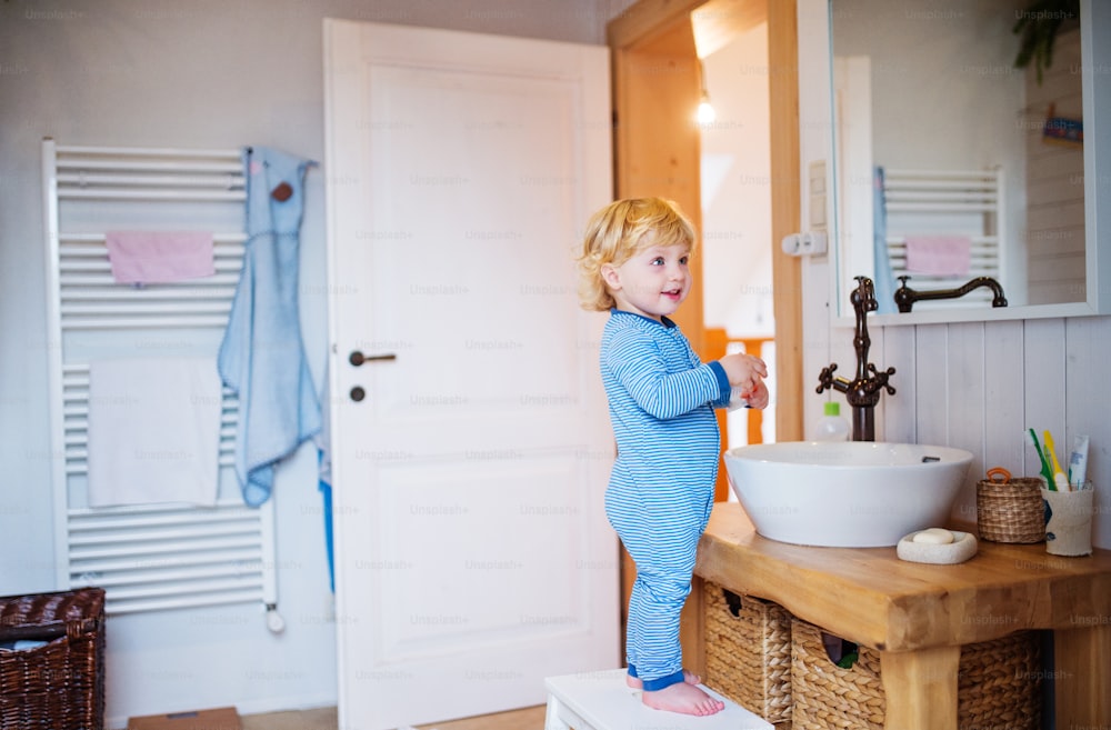 Cute toddler boy standing on a stool in front of mirror in the bathroom.