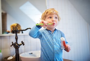 Lindo niño cepillándose los dientes en el baño. Niño pequeño parado en un taburete.