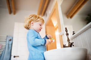Cute toddler brushing his teeth in the bathroom. Little boy standing on a stool in front of mirror.