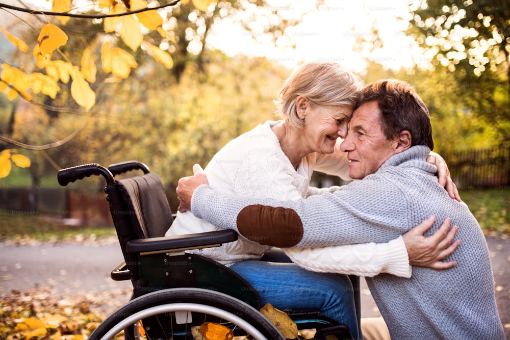 Senior couple in autumn nature. Man and woman in a wheelchair on a walk, hugging.