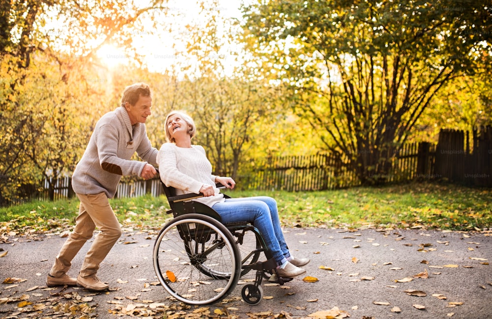 Senior couple in autumn nature. Man and woman in a wheelchair on a walk.