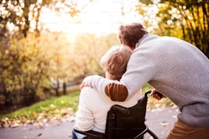 Senior couple in autumn nature. Man and woman in a wheelchair on a walk.