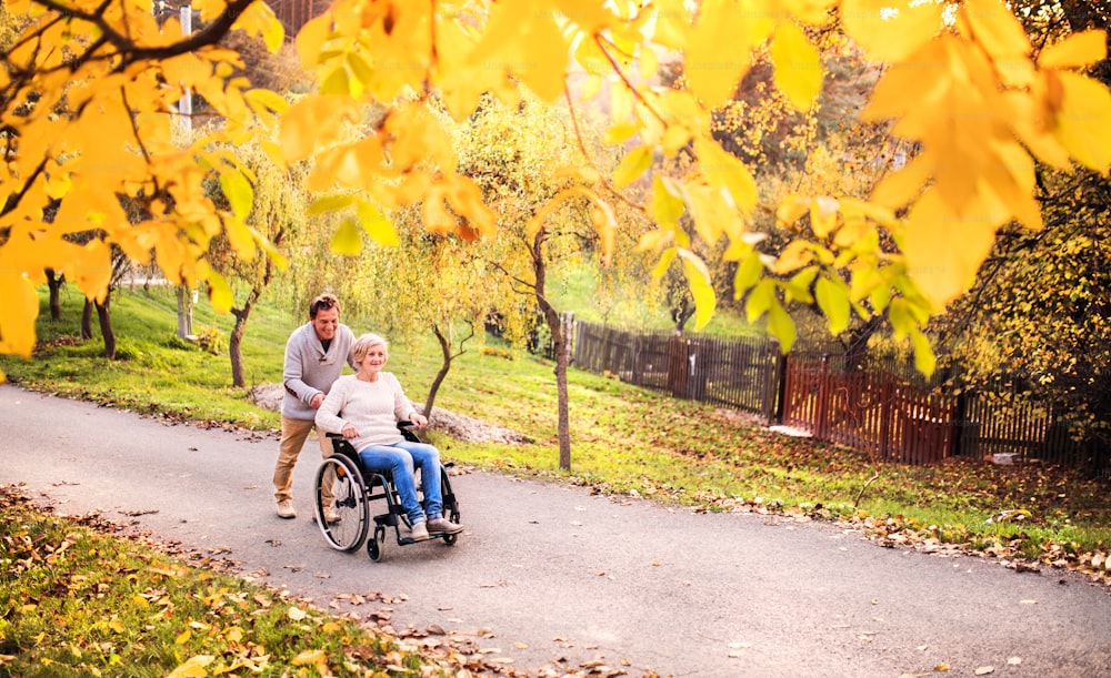 Pareja mayor en la naturaleza otoñal. Hombre y mujer en silla de ruedas en un paseo.