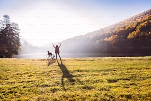 Femme âgée debout près du fauteuil roulant dans une nature automnale. Une femme se détend au bord du lac tôt le matin. Vue arrière.