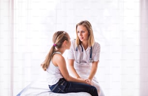 Young female doctor and a small girl in her office, talking.