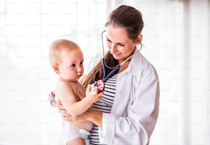 Young female doctor examining a baby with a stethoscope in her office.
