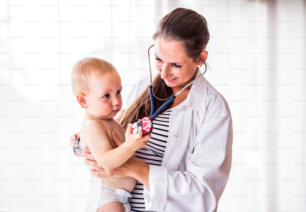 Young female doctor examining a baby with a stethoscope in her office.