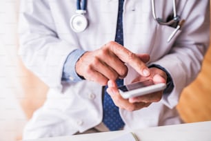 Medico maschio anziano irriconoscibile con smartphone in ufficio, messaggi di testo.