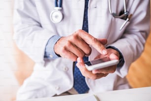 Nicht wiederzuerkennender leitender männlicher Arzt mit Smartphone in der Praxis, SMS.