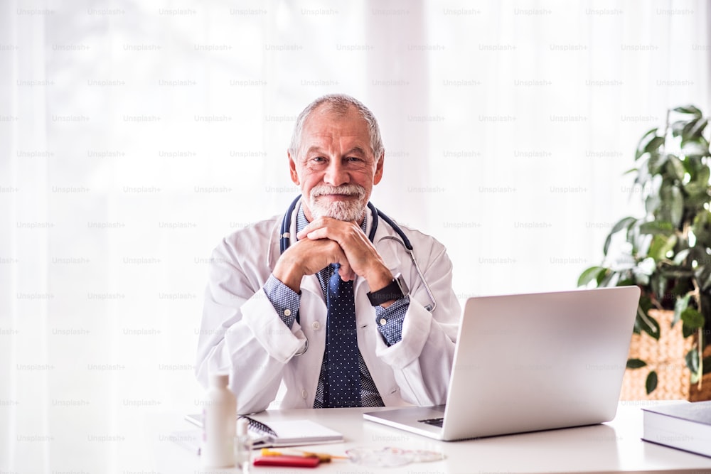 Senior male doctor with laptop sitting at the office desk.