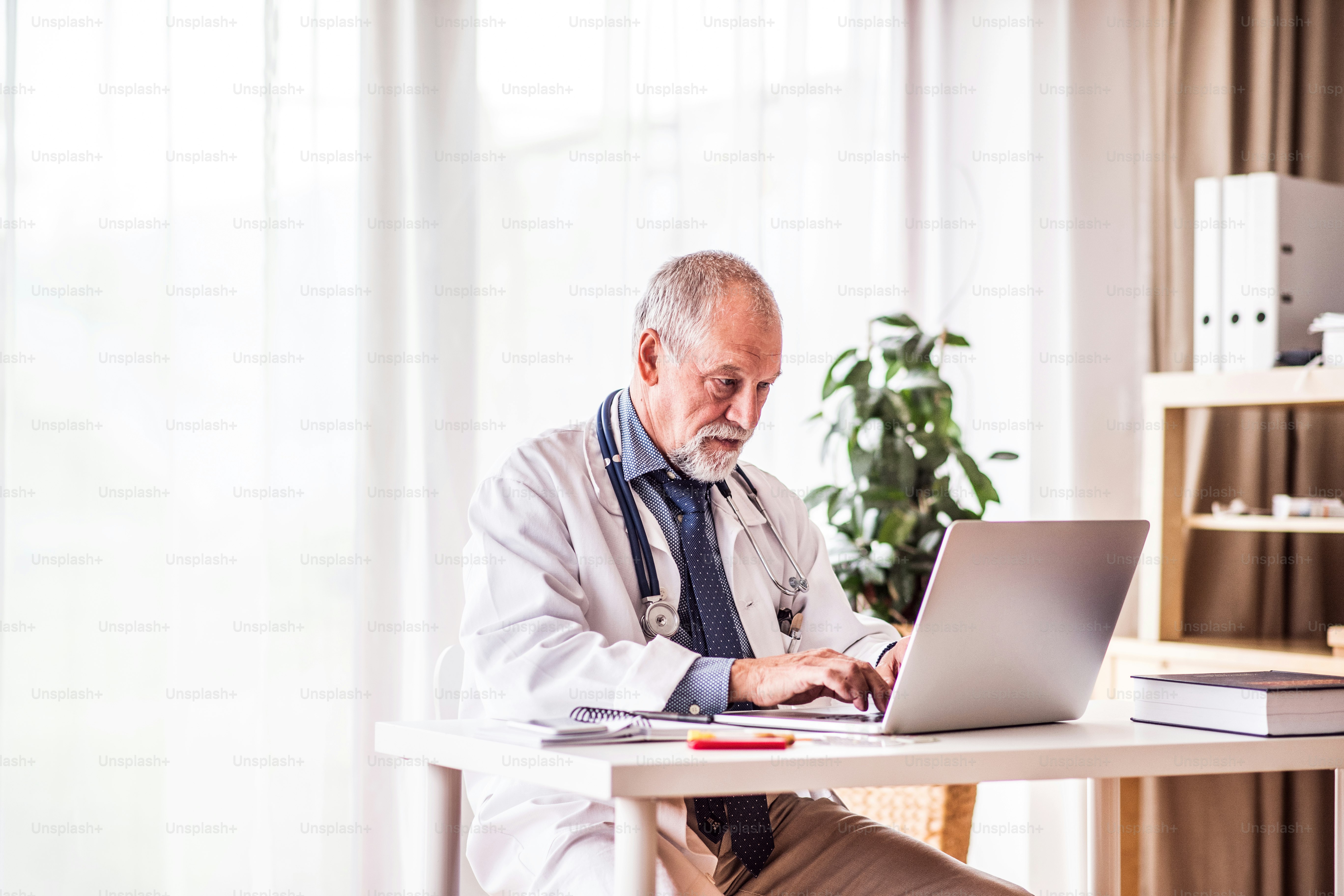 Médico senior trabajando en una computadora portátil en el escritorio de la oficina.