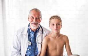 Retrato de um médico sênior do sexo masculino com estetoscópio e um menino pequeno em um consultório.