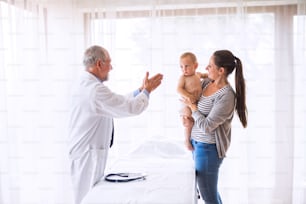 Senior male doctor , young mother and a baby boy in an office.