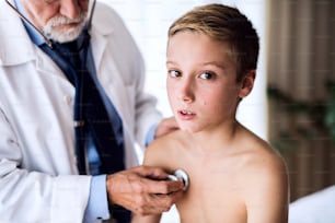 Unrecognizable senior male doctor examining a small boy with stethoscope in his office.