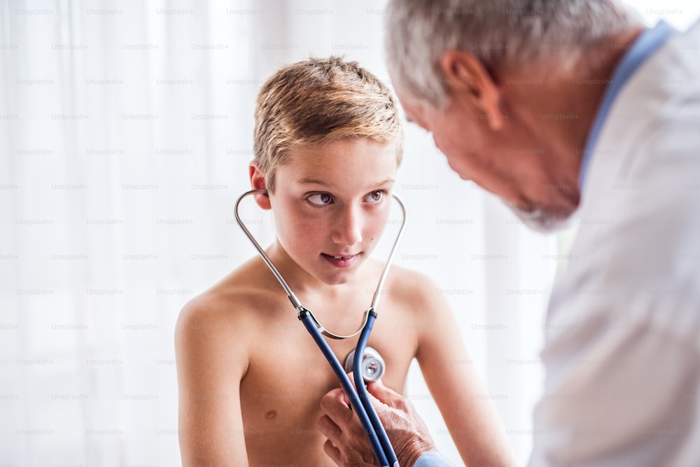Senior male doctor examining a small boy with stethoscope in his office.